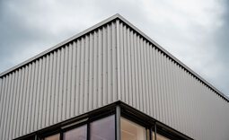 Eckansicht der Produktionshalle mit Attika und betontem Licht-Schatten-Verlauf.