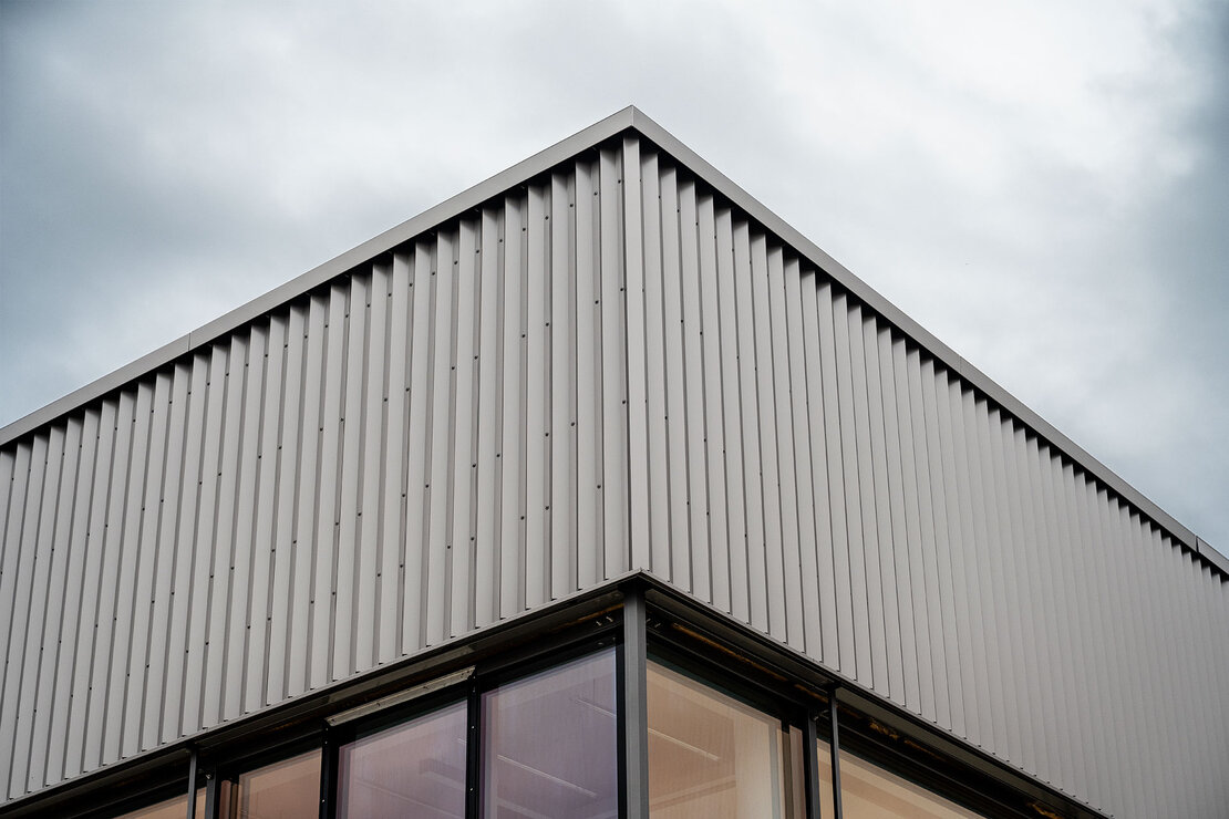 Eckansicht der Produktionshalle mit Attika und betontem Licht-Schatten-Verlauf.