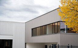 Außenansicht der Produktionshalle Pforzheim mit gleichmäßig strukturierter Designprofilfassade aus Stahl im Farbton ähnlich RAL 9006 Weißaluminium