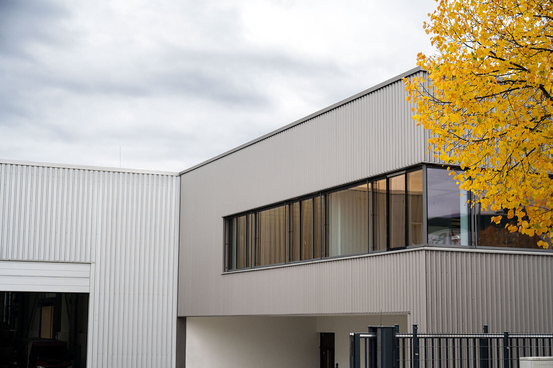 Außenansicht der Produktionshalle Pforzheim mit gleichmäßig strukturierter Designprofilfassade aus Stahl im Farbton ähnlich RAL 9006 Weißaluminium